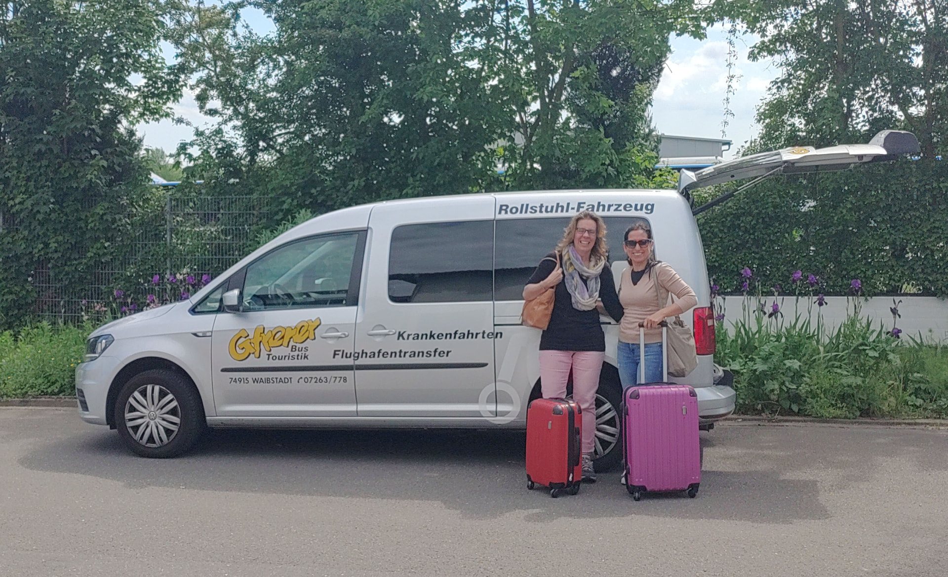 Zwei Reisende mit Koffern vor dem Gfrerer-Transferfahrzeug